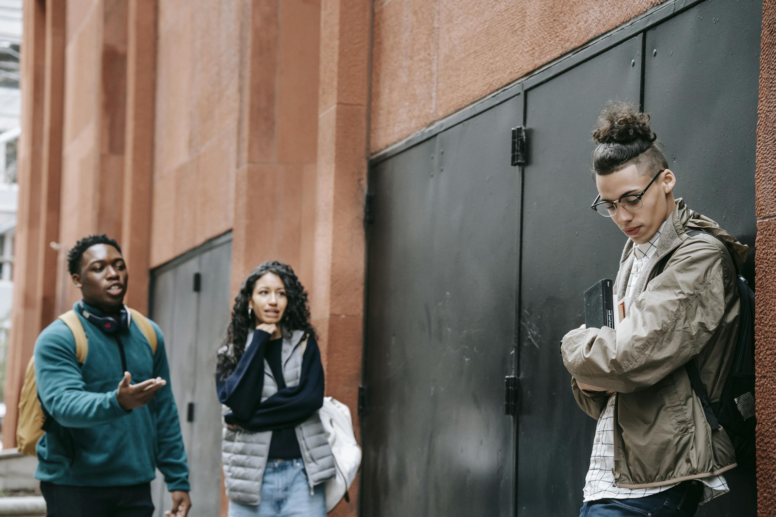 Bullied ethnic guy leaning on wall near rebellious multiracial classmates