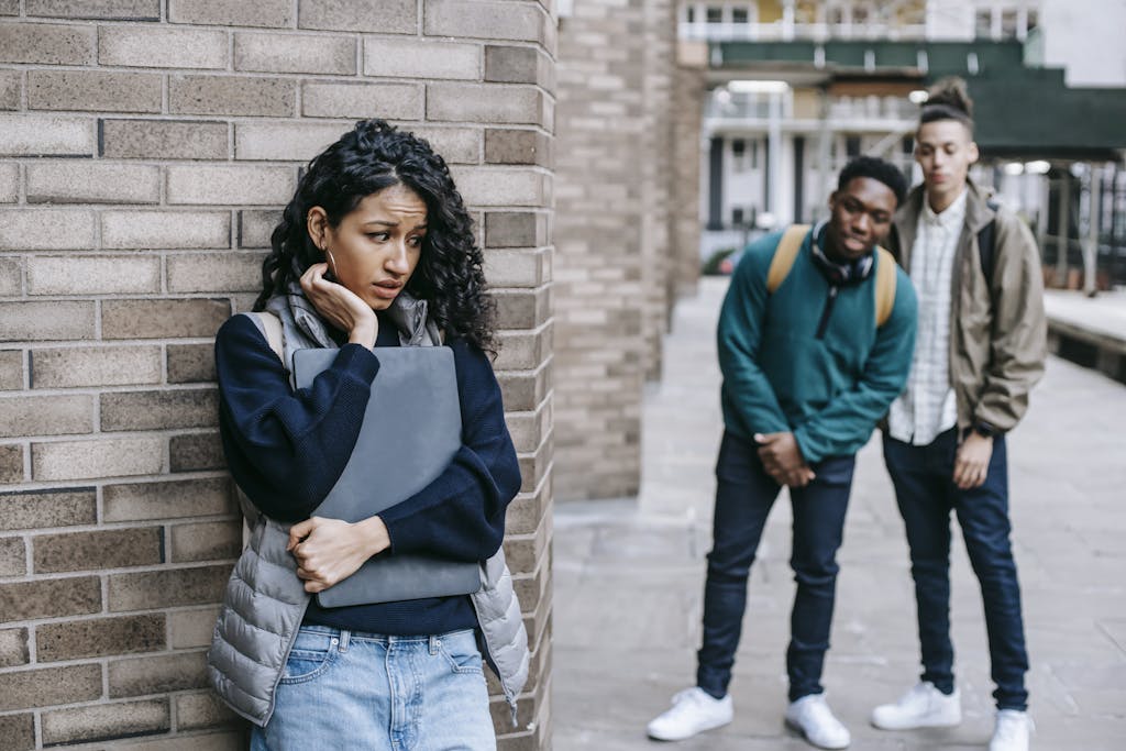 Latin American woman leaning on brick wall while hiding from multiracial classmates in college