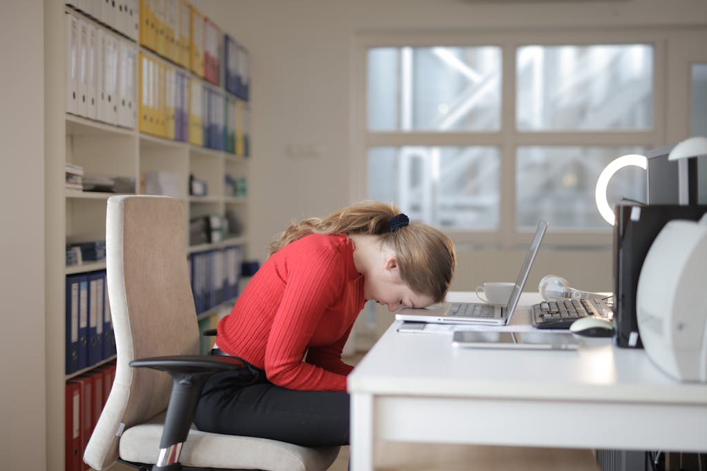 Woman in Red Long Sleeve Shirt Sitting on Chair While Leaning on Laptop